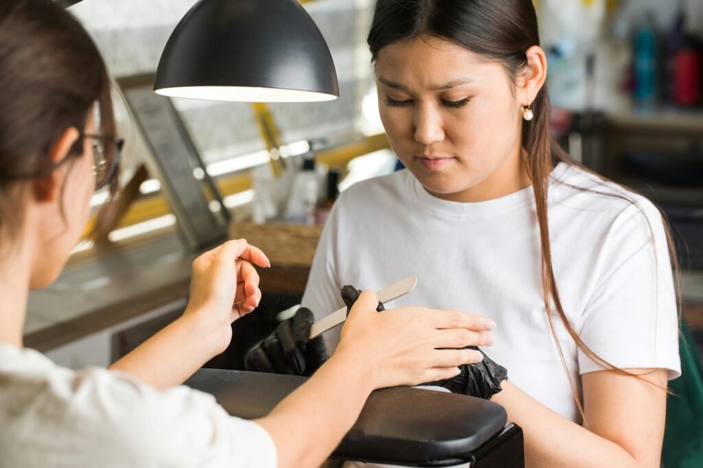 Manicurist processes nails of a client with a nail file in a beauty salon. Asian appearance